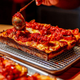 detroit style pizza being sauced